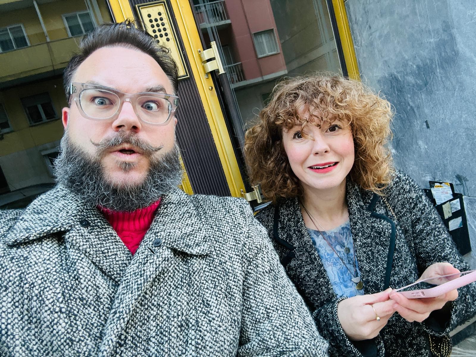 Man with beard and woman holding a phone looking into camera
