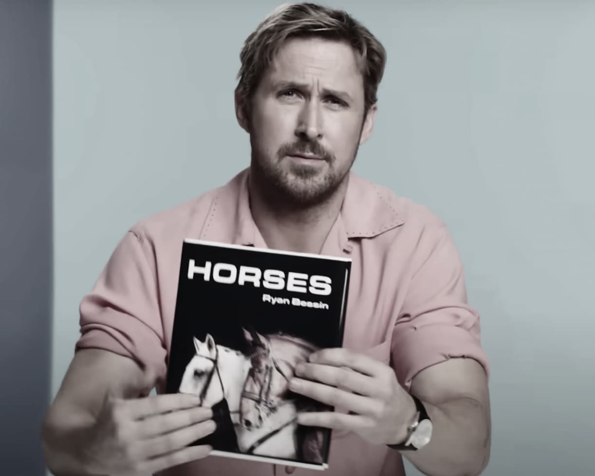 Ryan Gosling wearing a pink shirt and holding a book called Horses